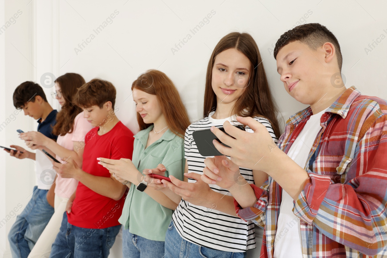 Teenagers with smartphones near white wall indoors Photo of Teenagers with smartphones near white wall indoors