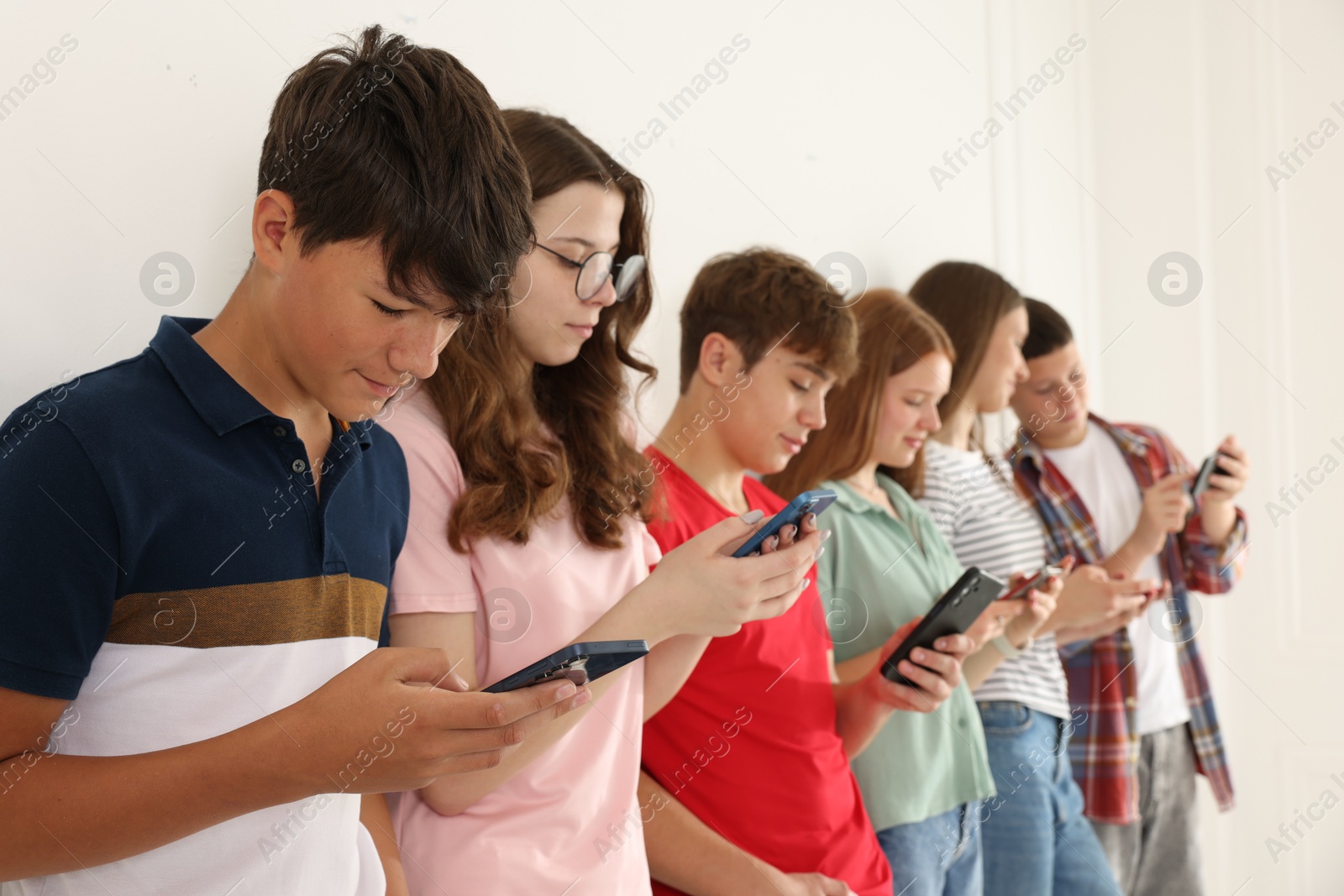 Teenagers with smartphones near white wall indoors Photo of Teenagers with smartphones near white wall indoors