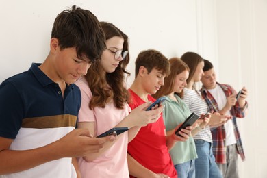 Photo of Teenagers with smartphones near white wall indoors