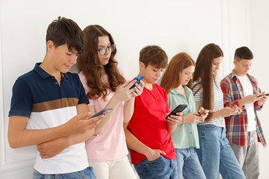 Photo of Teenagers with smartphones near white wall indoors