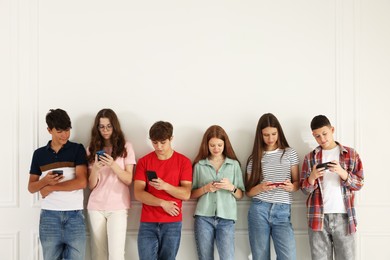 Photo of Teenagers with smartphones near white wall indoors