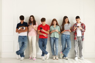 Photo of Teenagers with smartphones near white wall indoors