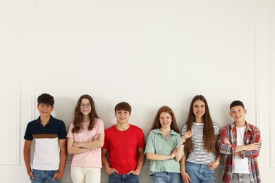 Photo of Group of happy teenagers posing near white wall indoors