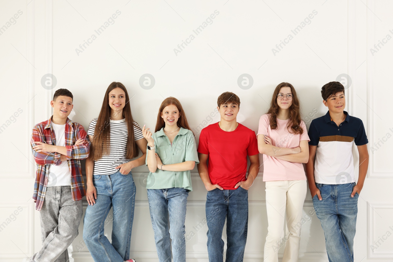 Photo of Group of happy teenagers posing near white wall indoors