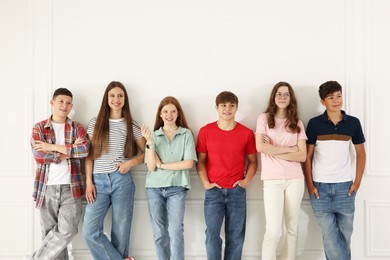 Photo of Group of happy teenagers posing near white wall indoors