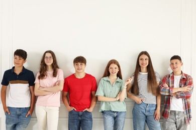 Photo of Group of happy teenagers posing near white wall indoors