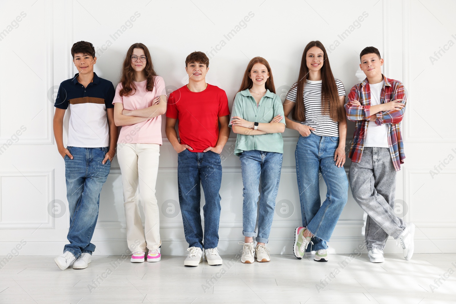 Group of happy teenagers posing near white wall indoors Photo of Group of happy teenagers posing near white wall indoors