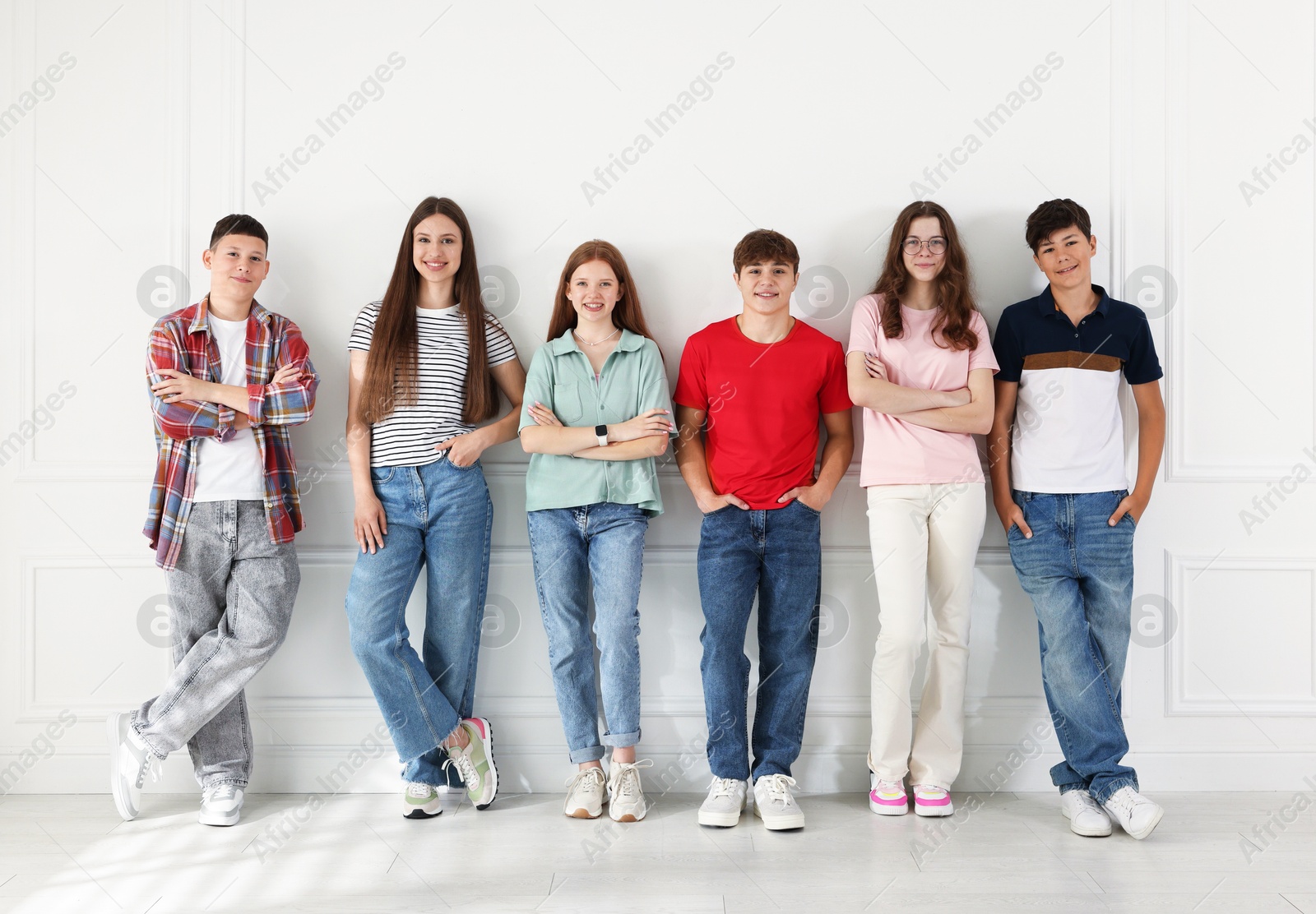 Photo of Group of happy teenagers posing near white wall indoors