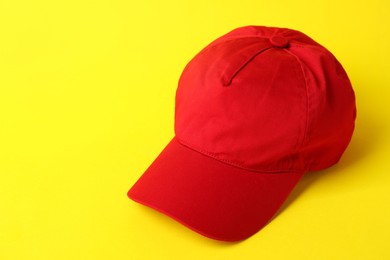 Photo of Red baseball hat on yellow background, closeup. Space for text