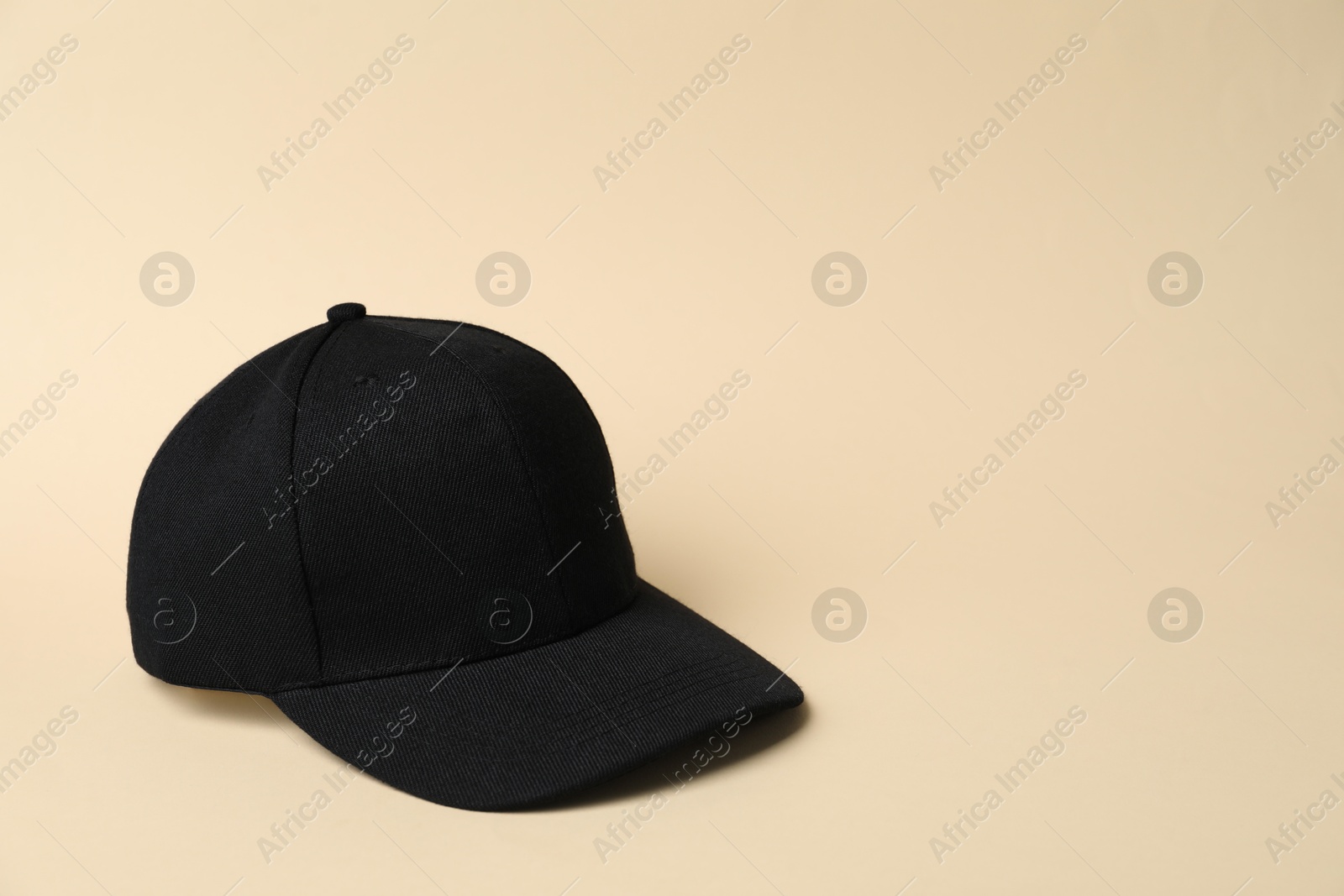 Black baseball hat on beige background, space for text Photo of Black baseball hat on beige background, space for text