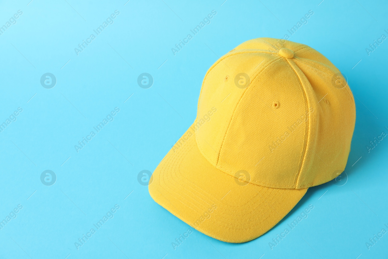 Photo of Yellow baseball hat on light blue background, above view. Space for text