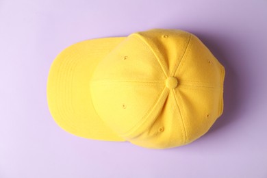 Photo of Yellow baseball hat on violet background, top view