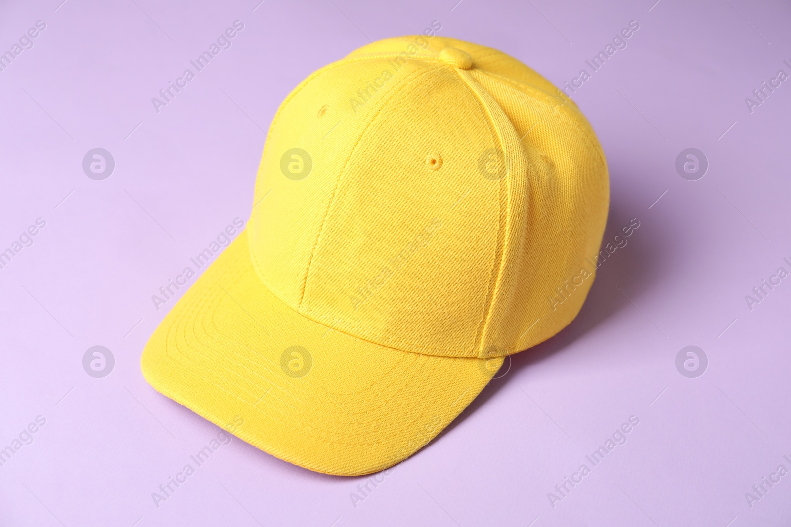 Photo of Yellow baseball hat on violet background, closeup. Mockup for design