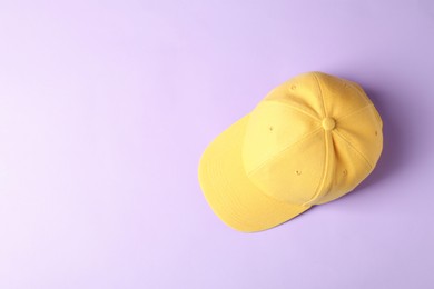 Photo of Yellow baseball hat on violet background, top view. Space for text