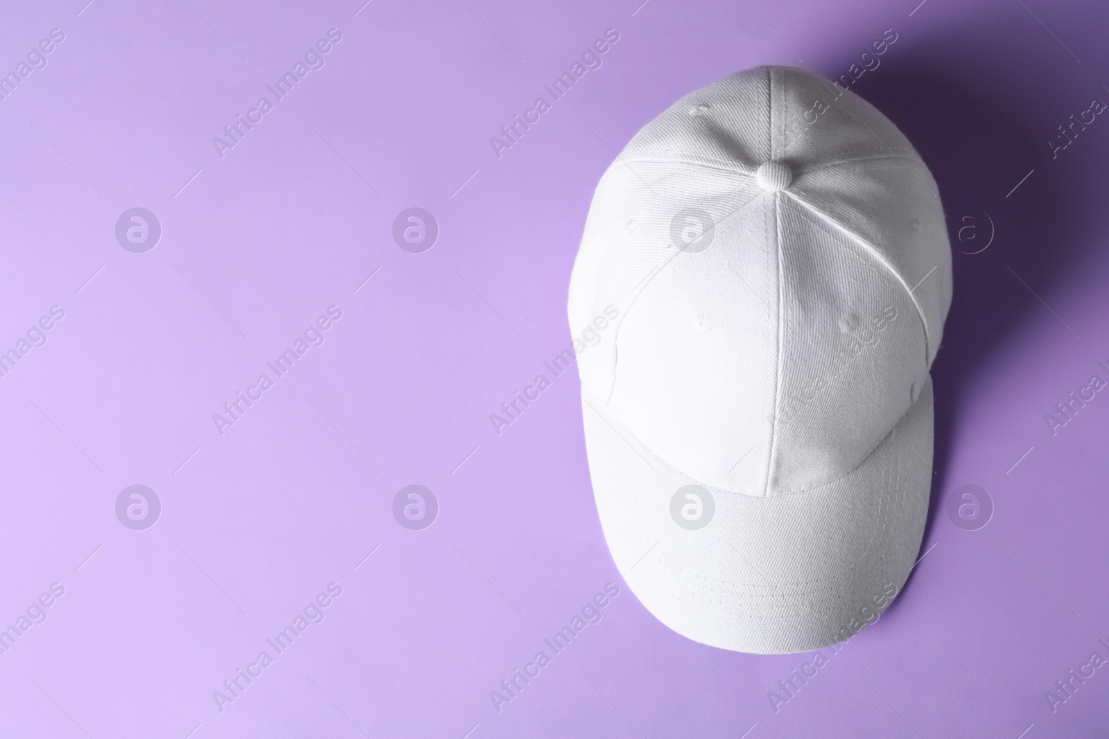 Photo of White baseball hat on violet background, top view. Space for text