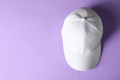 Photo of White baseball hat on violet background, top view. Space for text