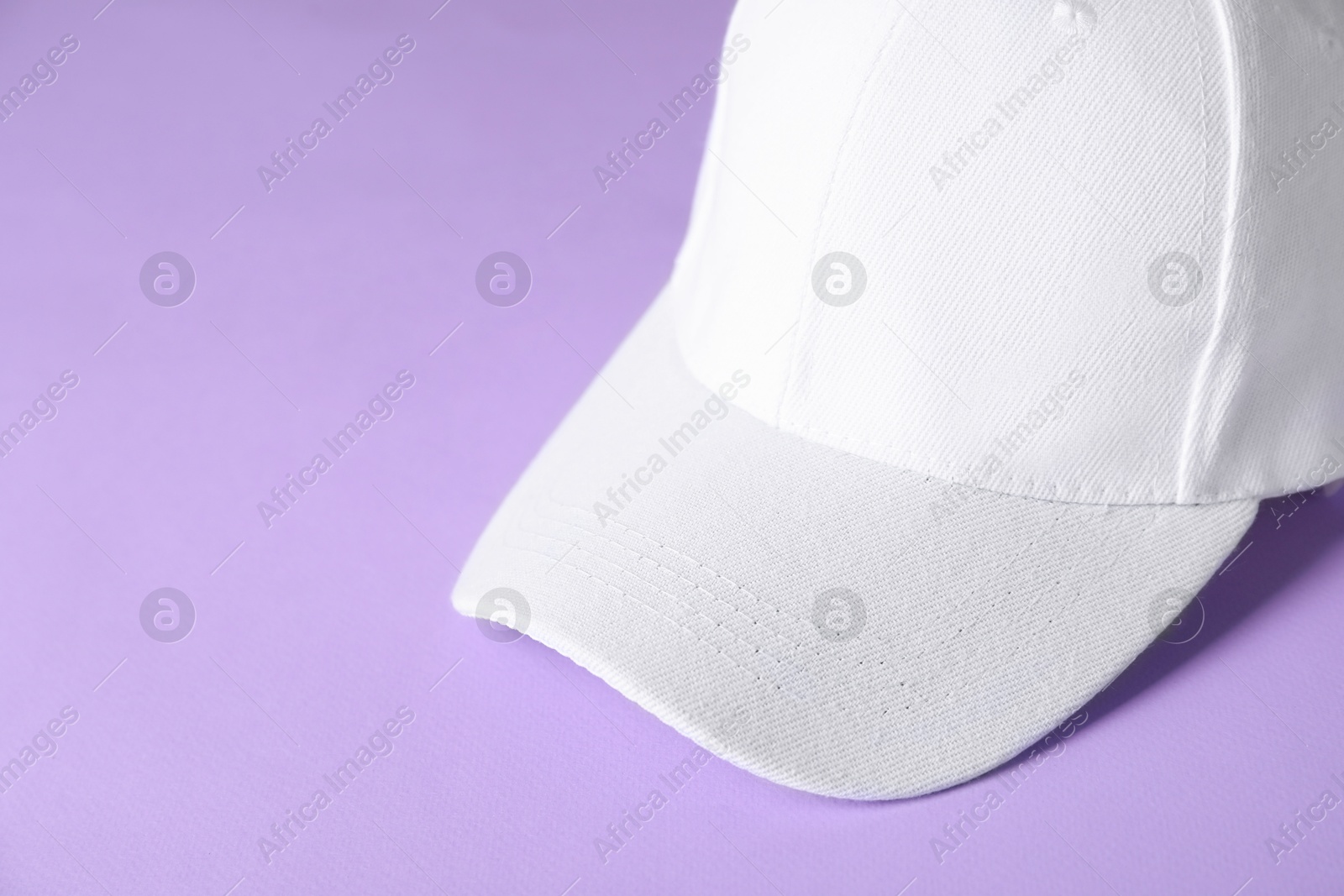 Photo of White baseball hat on violet background, closeup. Space for text