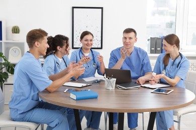 Photo of Medical students in uniforms studying together at table indoors