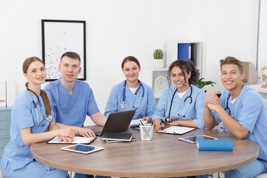 Photo of Medical students in uniforms studying together at table indoors