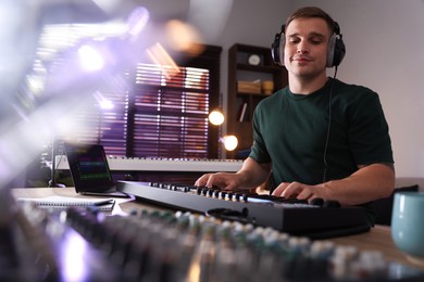 Photo of Man in headphones working with MIDI keyboard at table in home studio, low angle view