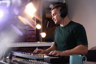 Photo of Man in headphones working with MIDI keyboard at table in home studio