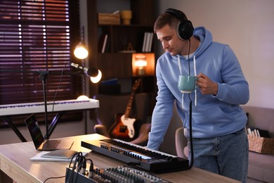 Photo of Man in headphones working with MIDI keyboard at table in home studio