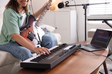 Photo of Smiling woman working with MIDI keyboard and guitar at table in home studio, selective focus
