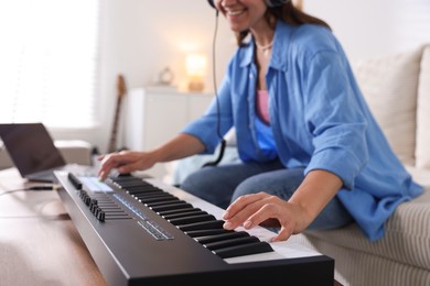 Photo of Smiling woman working with MIDI keyboard at table in home studio, closeup