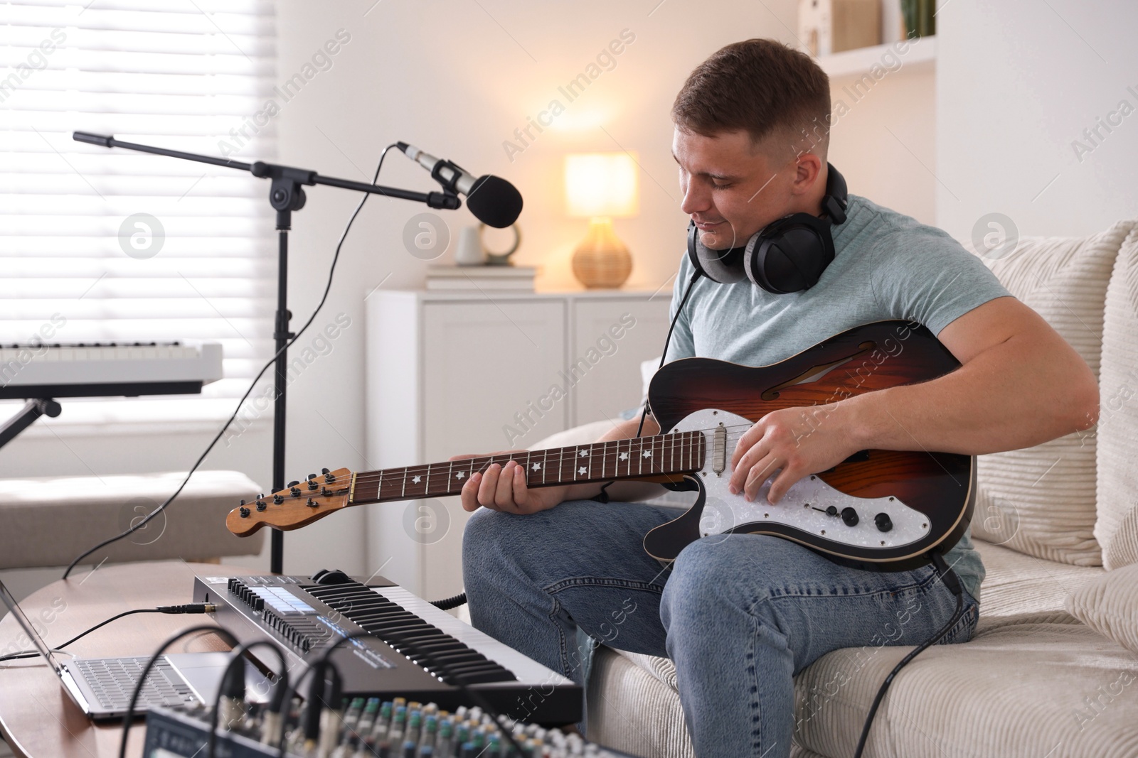 Man working with guitar and MIDI keyboard on sofa in home studio Photo of Man working with guitar and MIDI keyboard on sofa in home studio