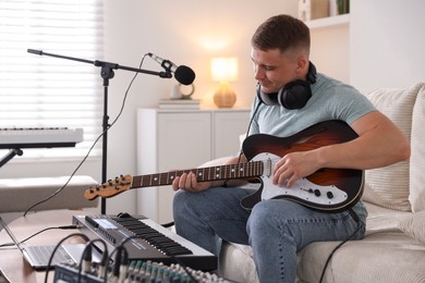 Photo of Man working with guitar and MIDI keyboard on sofa in home studio