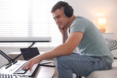 Photo of Man in headphones working with MIDI keyboard at table indoors
