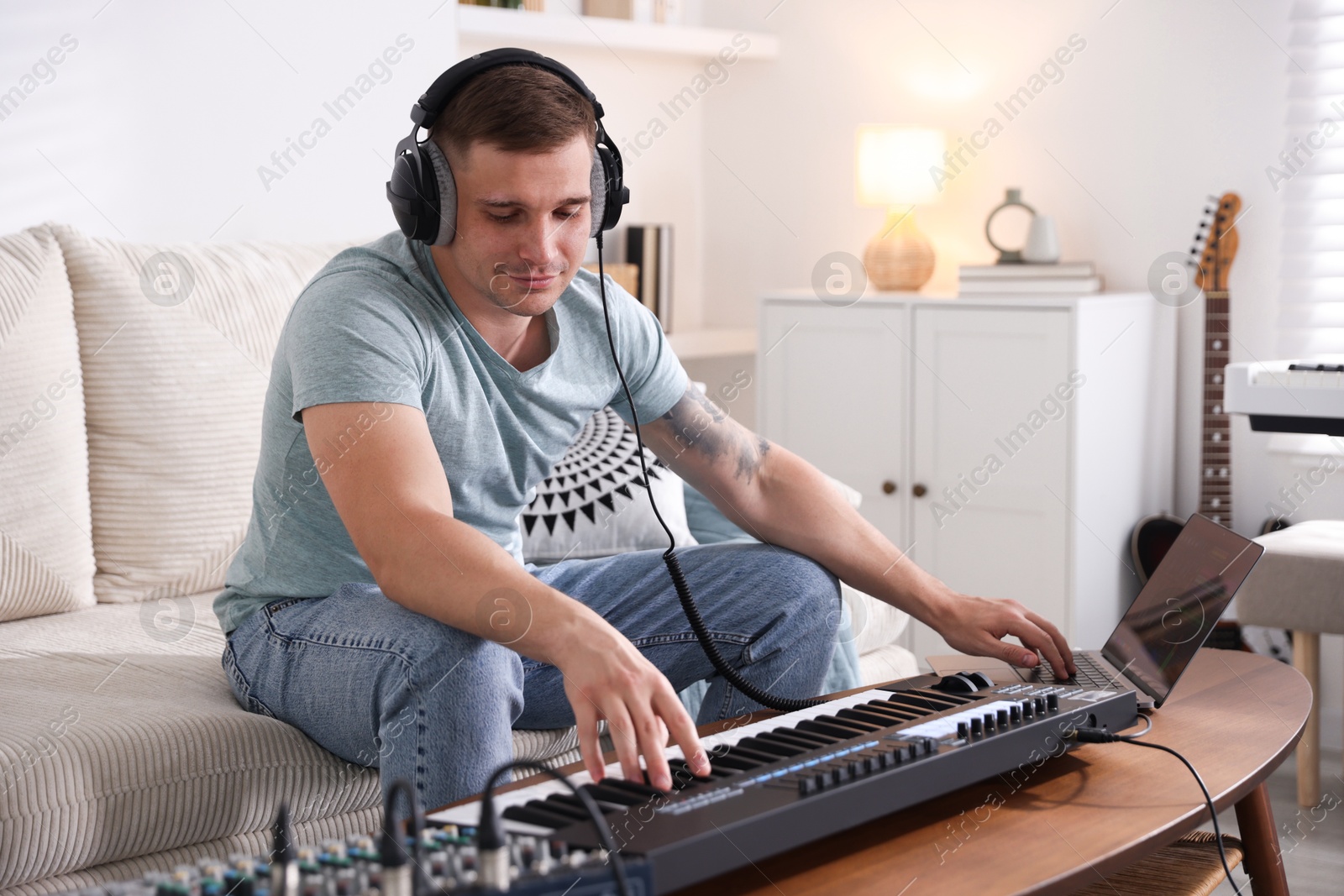Man in headphones working with MIDI keyboard and laptop at table indoors Photo of Man in headphones working with MIDI keyboard and laptop at table indoors