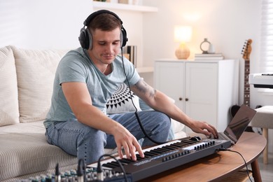 Photo of Man in headphones working with MIDI keyboard and laptop at table indoors