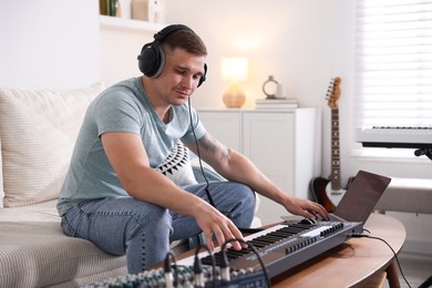 Photo of Man in headphones working with MIDI keyboard and laptop at table indoors