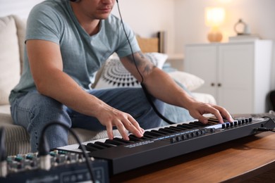 Photo of Man working with MIDI keyboard at table indoors, closeup
