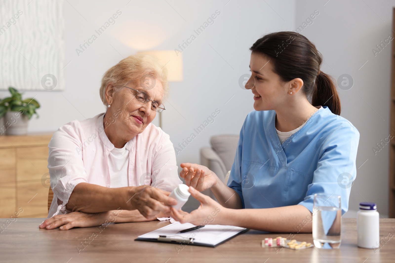 Nurse giving pills to senior woman at wooden table indoors. Home health care service Photo of Nurse giving pills to senior woman at wooden table indoors. Home health care service