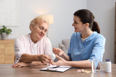 Photo of Nurse giving pills to senior woman at wooden table indoors. Home health care service