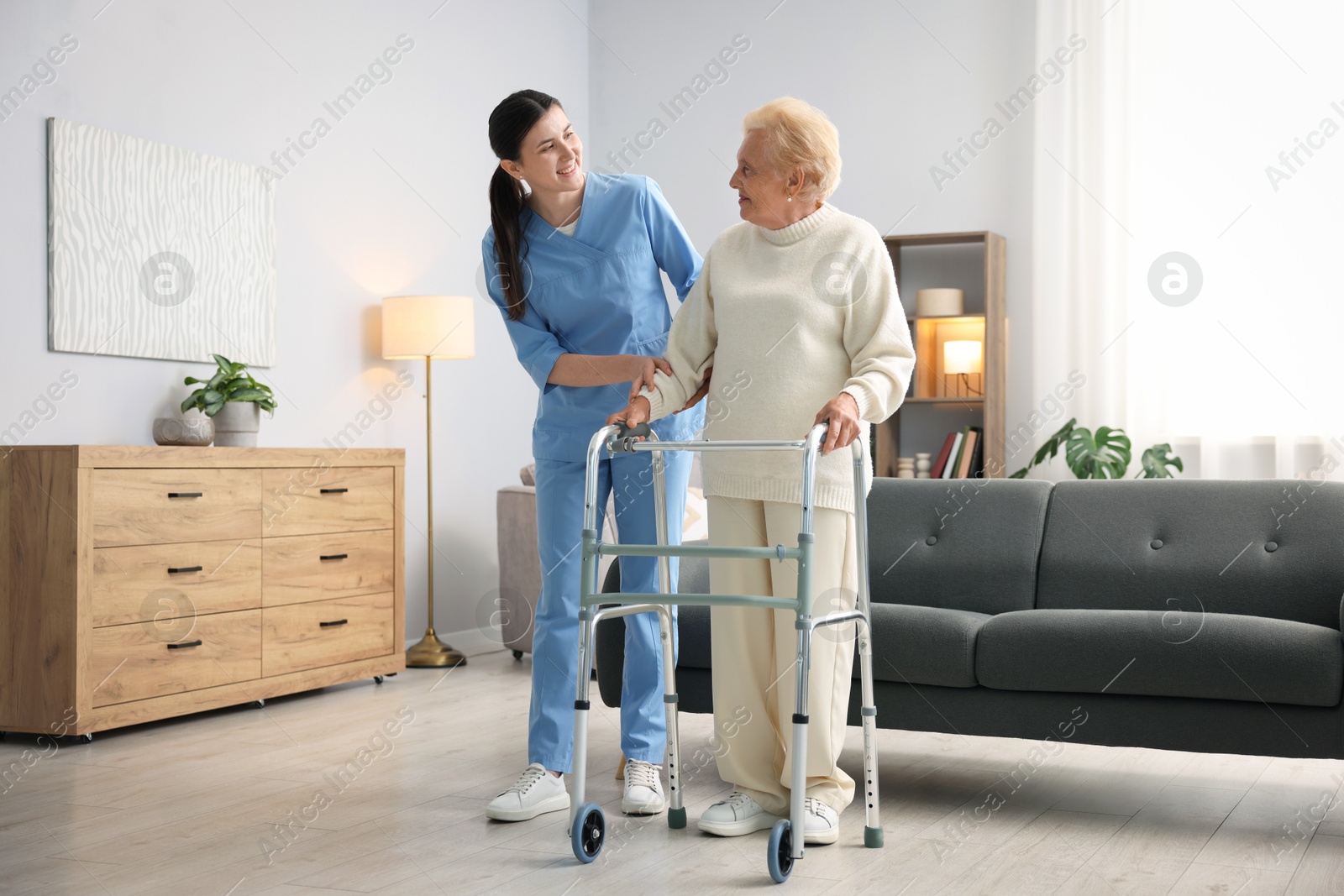 Photo of Nurse assisting senior woman with walking frame indoors. Home health care service