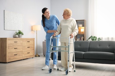 Photo of Nurse assisting senior woman with walking frame indoors. Home health care service