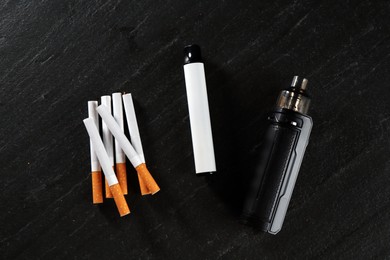 Photo of Electronic smoking devices and cigarettes on black table, flat lay