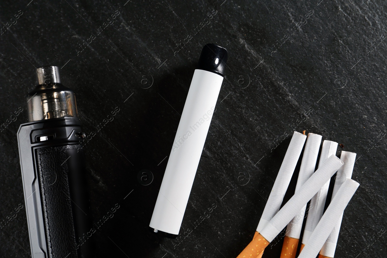 Electronic smoking devices and cigarettes on black table, flat lay Photo of Electronic smoking devices and cigarettes on black table, flat lay