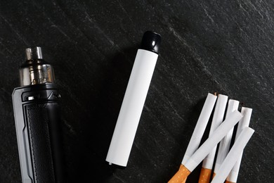 Photo of Electronic smoking devices and cigarettes on black table, flat lay