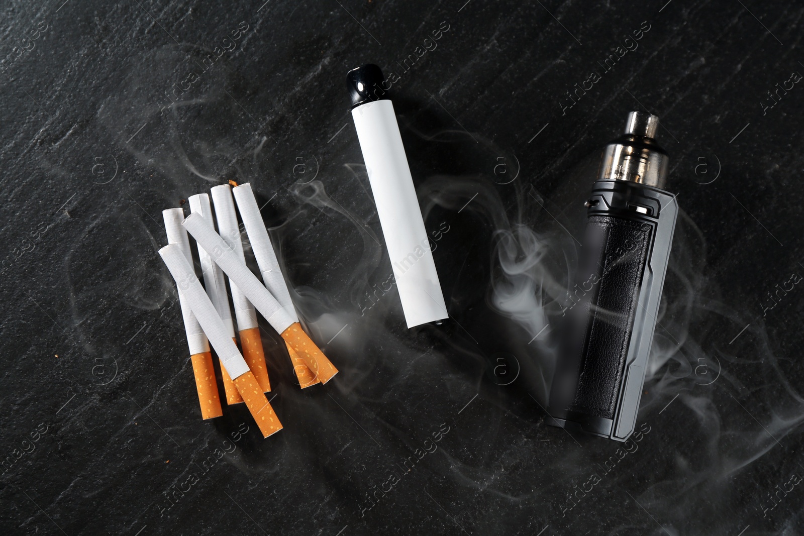 Electronic smoking devices and cigarettes on black table, flat lay Photo of Electronic smoking devices and cigarettes on black table, flat lay