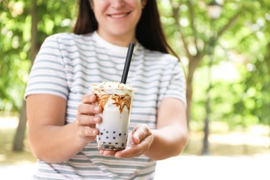Photo of Woman with tasty milk bubble tea in plastic cup outdoors, closeup