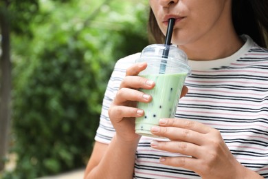 Photo of Woman drinking tasty milk bubble tea from plastic cup outdoors, closeup. Space for text