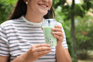 Photo of Woman with tasty milk bubble tea in plastic cup outdoors, closeup