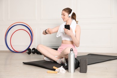 Photo of Woman checking fitness tracker during training indoors