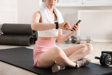 Photo of Woman checking fitness tracker during training indoors, closeup