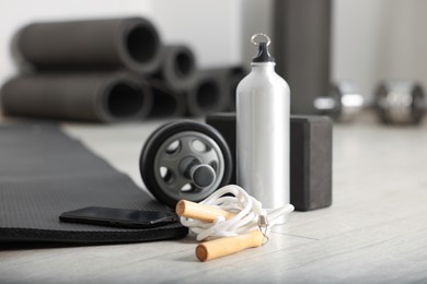 Photo of Phone and different fitness equipment on floor in gym, closeup
