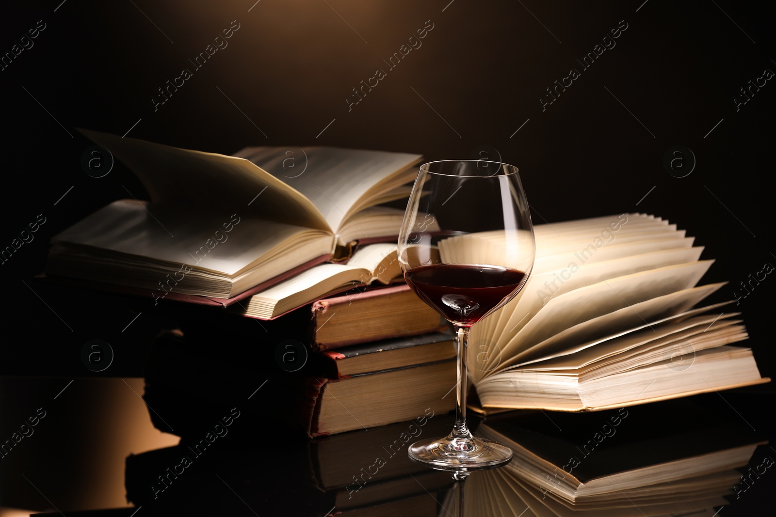 Red wine in glass and stack of books on mirror table against dark background, closeup Photo of Red wine in glass and stack of books on mirror table against dark background, closeup